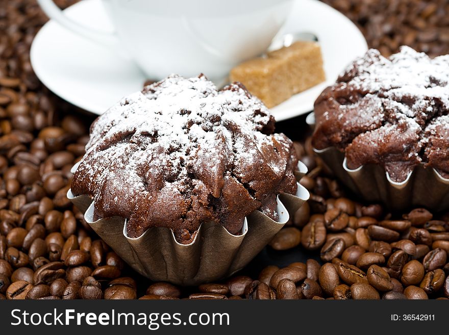 Chocolate muffin and cappuccino on coffee beans, close-up