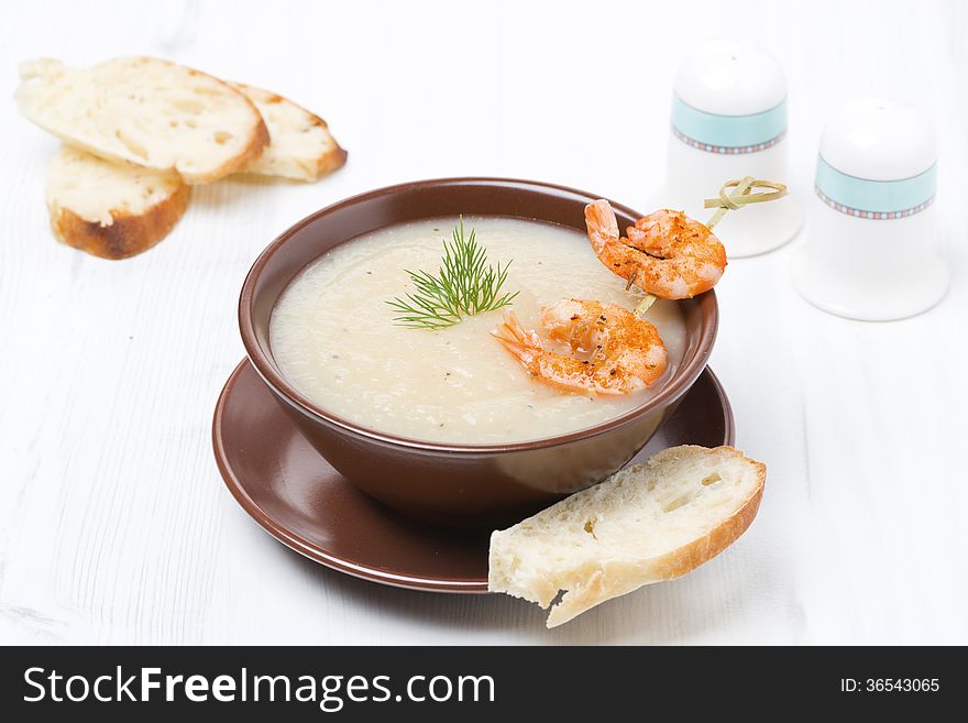 Potato cream soup with glazed shrimp and bread in a bowl, close-up