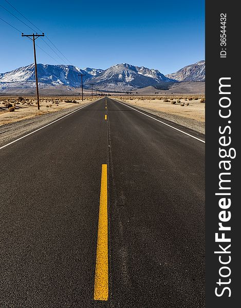 Single yellow line in middle of road leading to the mountains with telephone poles on one side. Single yellow line in middle of road leading to the mountains with telephone poles on one side