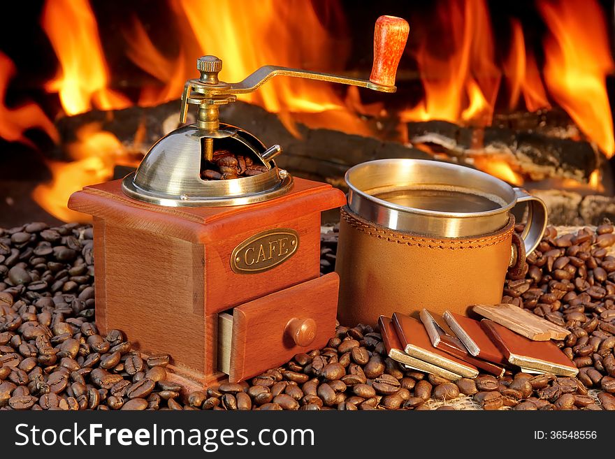 Coffee Mug, chocolate, and coffee grinder on the scattered coffee beans at the fireplace. Coffee Mug, chocolate, and coffee grinder on the scattered coffee beans at the fireplace