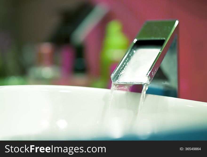 Water runs out of tap, corner of modern bathroom with cosmetics on the background, blurred