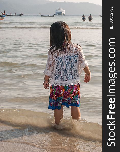 Backview of a caucasian white girl child with long blond hair standing and playing in the water of the Phuket on a beach in Thailand during summer holidays. Backview of a caucasian white girl child with long blond hair standing and playing in the water of the Phuket on a beach in Thailand during summer holidays.