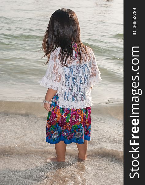 Backview of a caucasian white girl child with long blond hair standing and playing in the water of the Phuket on a beach in Thailand during summer holidays. Backview of a caucasian white girl child with long blond hair standing and playing in the water of the Phuket on a beach in Thailand during summer holidays.