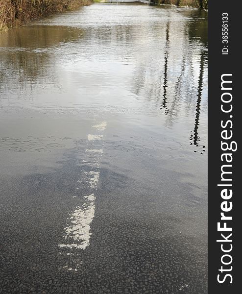 A country road is closed as a swollen river breaks its banks. Hampshire, England UK Low perspective, reflections, submerged road marking. A country road is closed as a swollen river breaks its banks. Hampshire, England UK Low perspective, reflections, submerged road marking.