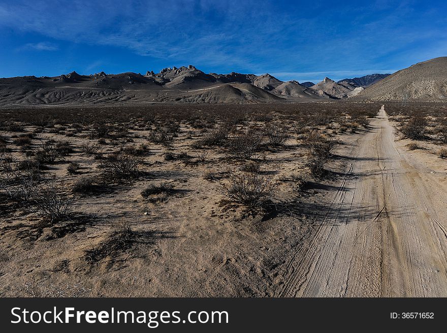 Dirt road leads to mountains through desert