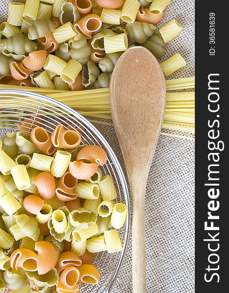Wooden spoon and uncooked pasta on natural fabric