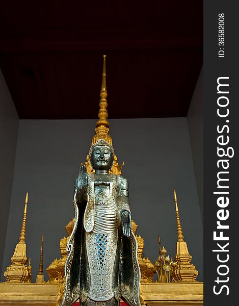 The metal standing Buddha with golden pagoda in the temple in Th