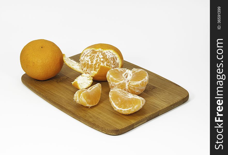 Clementine oranges, peeled and unpeeled, on a bamboo cutting board against a white background. Clementine oranges, peeled and unpeeled, on a bamboo cutting board against a white background