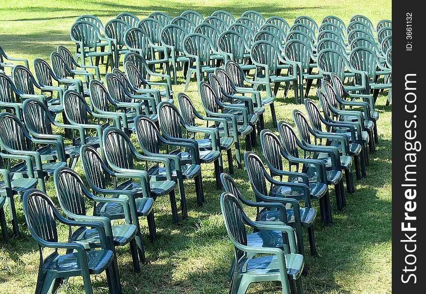 Ranks of empty green plastic outdoor chairs arrayed on lawn in full sunlight. Ranks of empty green plastic outdoor chairs arrayed on lawn in full sunlight