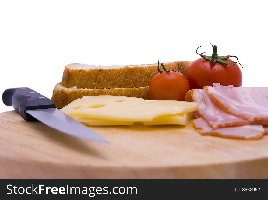 A cutting board with sandwich ingredients (swiss cheese, bacon, tomatoes, bread) and a knife. A cutting board with sandwich ingredients (swiss cheese, bacon, tomatoes, bread) and a knife.