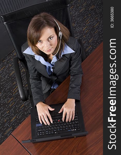 Young attractive brunette call center agent talking on the headset in a modern office setting with laptop. Young attractive brunette call center agent talking on the headset in a modern office setting with laptop