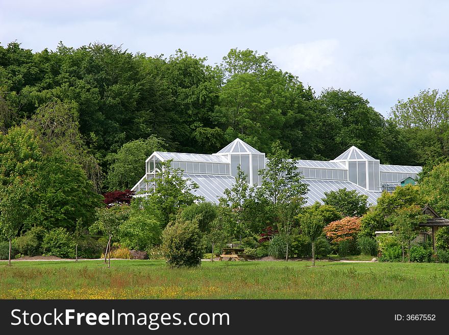 Large white greenhouse set amidst gardens of trees, shrubs and flowers. Large white greenhouse set amidst gardens of trees, shrubs and flowers.