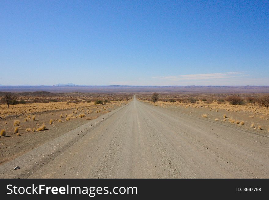 Straight endless gravel road through the namibian desert