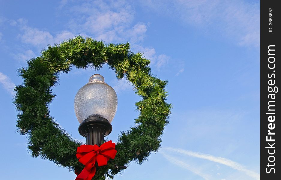 Evergreen wreath with a red ribbon hanging from a street light on a bright sunny day. Evergreen wreath with a red ribbon hanging from a street light on a bright sunny day