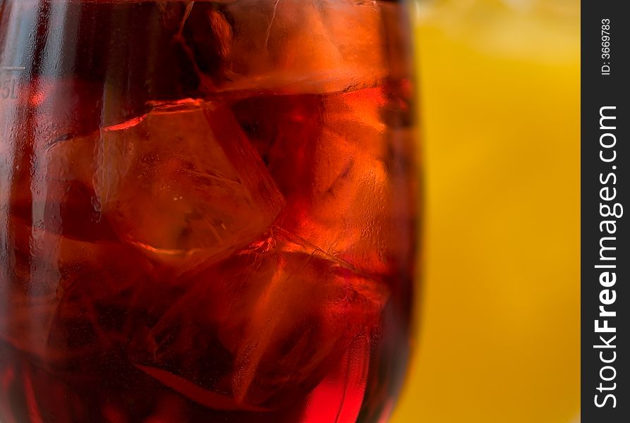 Abstract of ice cubes floating in a backlighted glass of fruit juice against another glass of orange juice. Abstract of ice cubes floating in a backlighted glass of fruit juice against another glass of orange juice