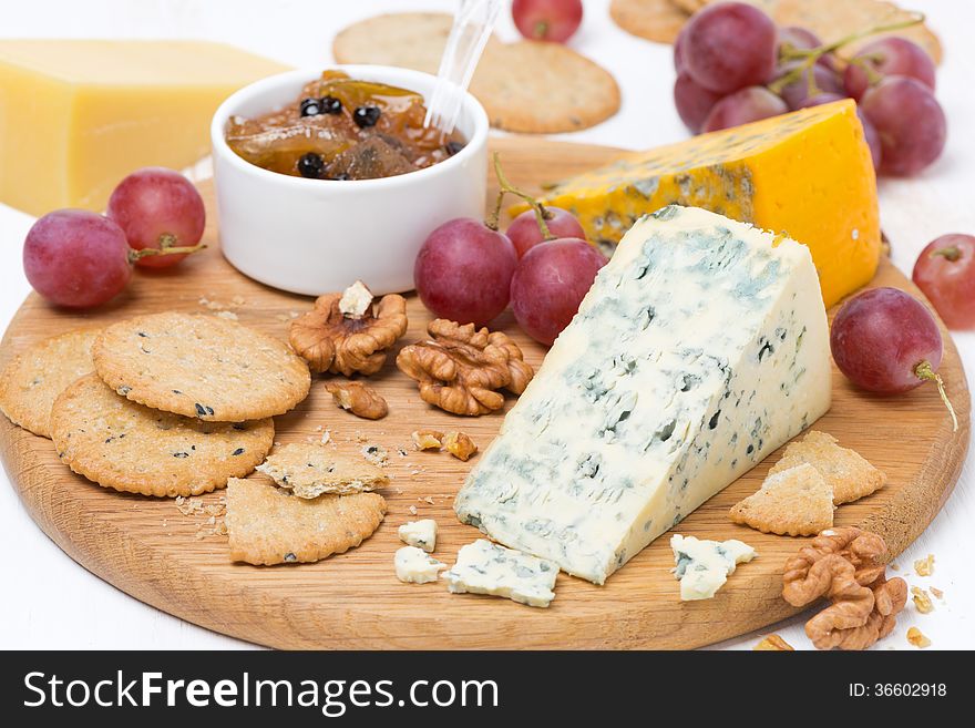 Assorted cheeses with mold, grapes, crackers, jam and nuts on a wooden board, close-up