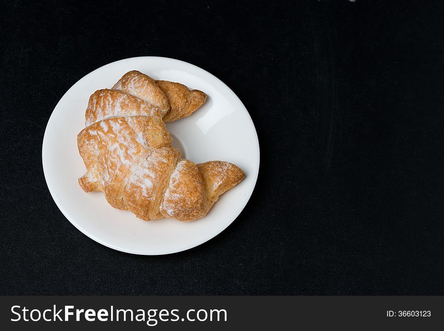 Fresh croissant on a plate on black background, top view, close-up