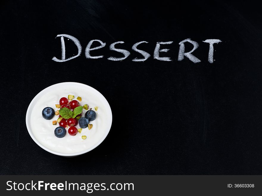 Yogurt with fresh berries on a black background and word dessert