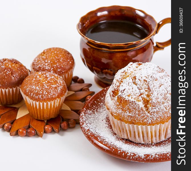 Fresh muffins with powdered sugar on a white background with a cup of coffee