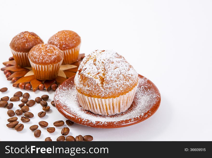 Fresh muffins with powdered sugar and coffee beans on a white background
