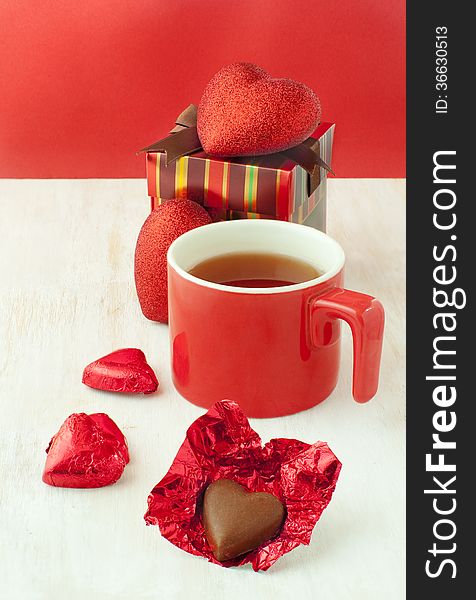 Heart shaped chocolates a cup of tea in a red cup and a gift box. Heart shaped chocolates a cup of tea in a red cup and a gift box