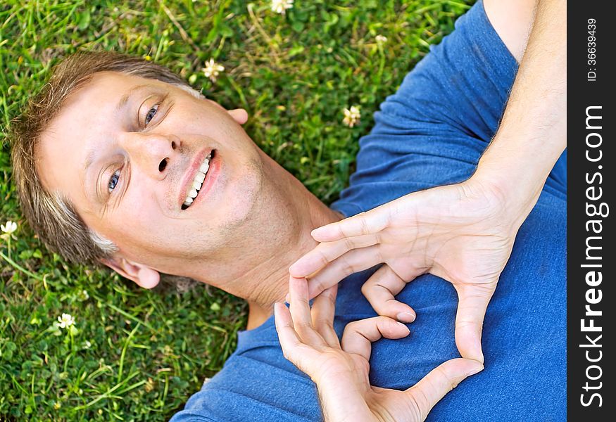 Man lying on grass showing a heart with his hands. Man lying on grass showing a heart with his hands