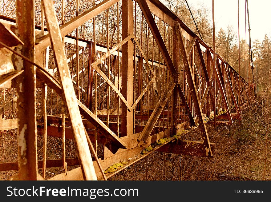 The photo shows an outdated rusty bridge in the forest.