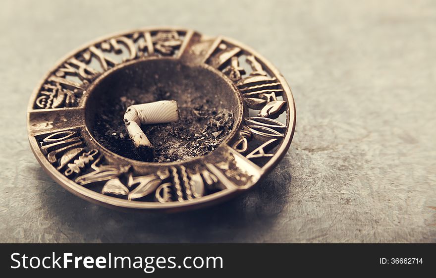 Details of cigarette in oriental metal ashtray. Details of cigarette in oriental metal ashtray.