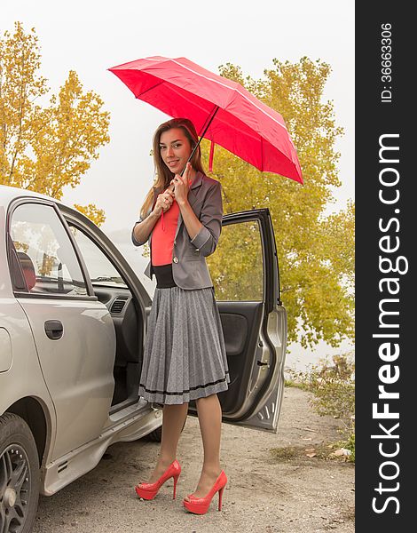 Happy woman outdoor in autamn with red umbrella near the car. Happy woman outdoor in autamn with red umbrella near the car