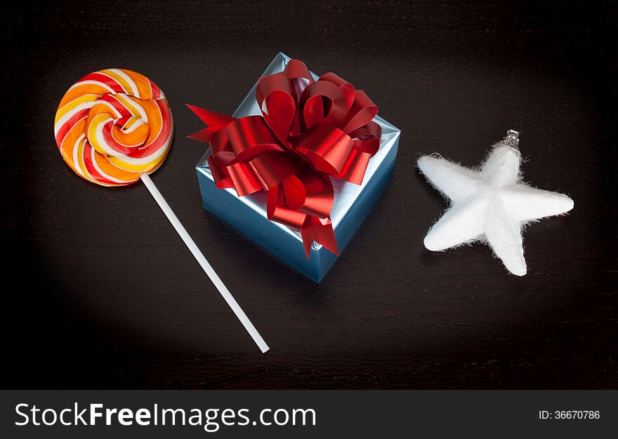 Blue gift box, candycane and white christmas star on black wooden background