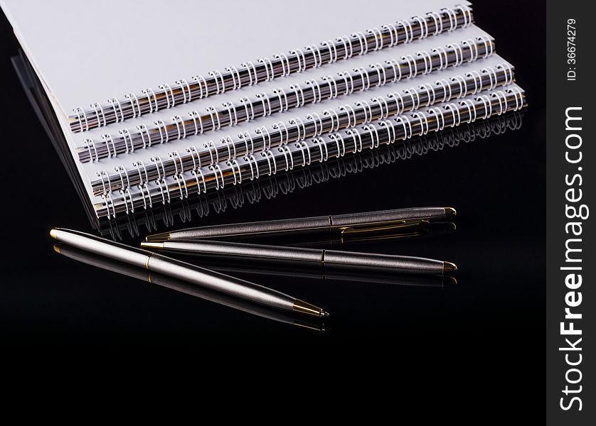 Image of three notebooks and three pens on a black background