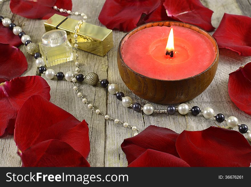 Big red candle with jewelry and rose petals on wood