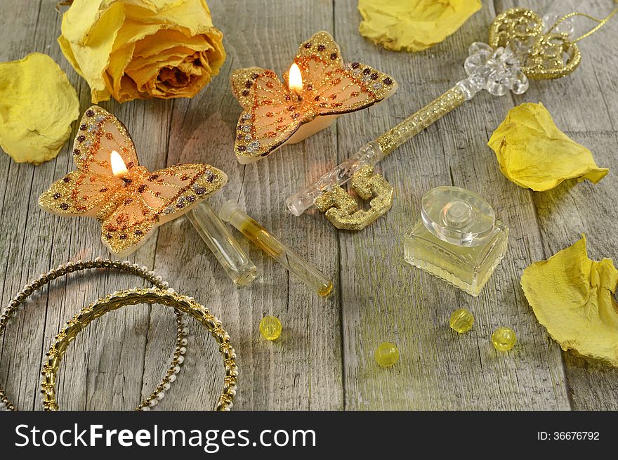 Still life with yellow perfume, the golden key, butterfly candles and jewelry on wood. Still life with yellow perfume, the golden key, butterfly candles and jewelry on wood