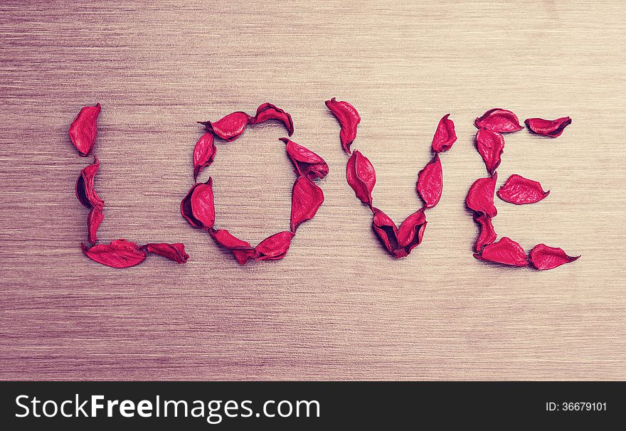 Background Valentine's Day. word love petals of red roses on a wooden board. Background Valentine's Day. word love petals of red roses on a wooden board