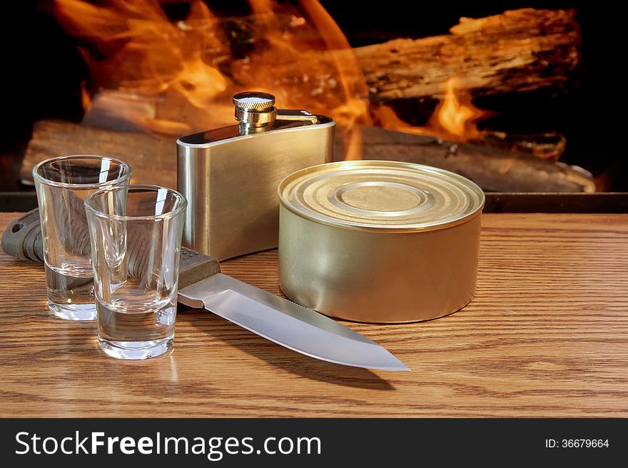 Hunting Knife, Canned Food, Hip Flask and two Short-glasses near the Open Fireplace. Hunting Knife, Canned Food, Hip Flask and two Short-glasses near the Open Fireplace