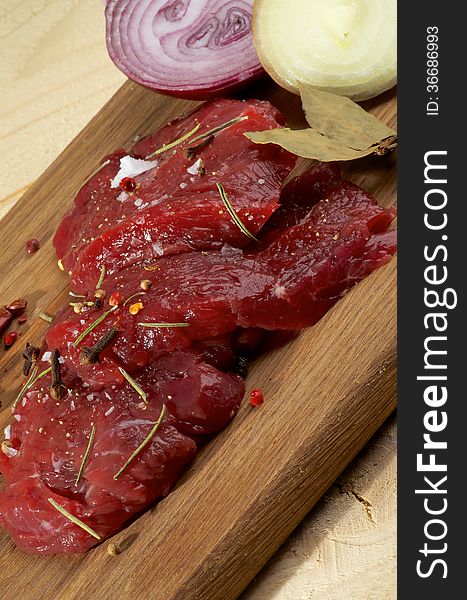 Arrangement of Raw Sliced Beef with Halves of White and Red Onion and Spices closeup on Wooden Cutting Board. Arrangement of Raw Sliced Beef with Halves of White and Red Onion and Spices closeup on Wooden Cutting Board