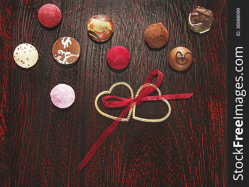 Colorful pralines candies with two hearts and ribbon wooden floor