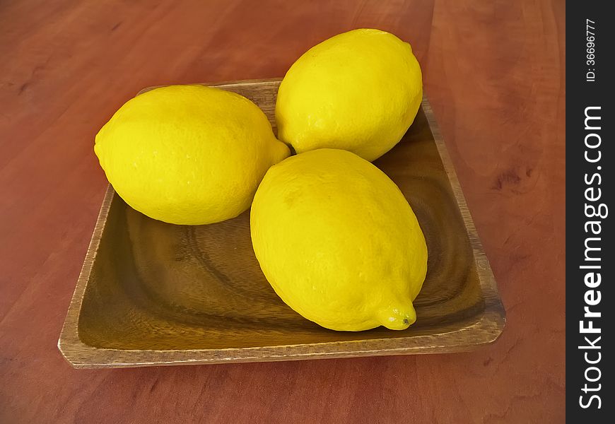 Three fresh lemons on a wooden plate on a table.