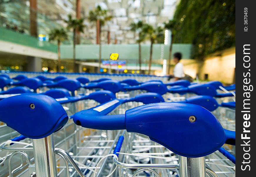 Luggage trolleys all parked and ready for use at the luggage collection area in an airport's arrival hall.