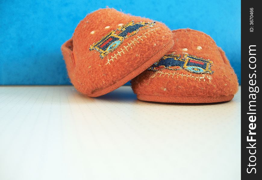 Orange worn baby slippers against blue background