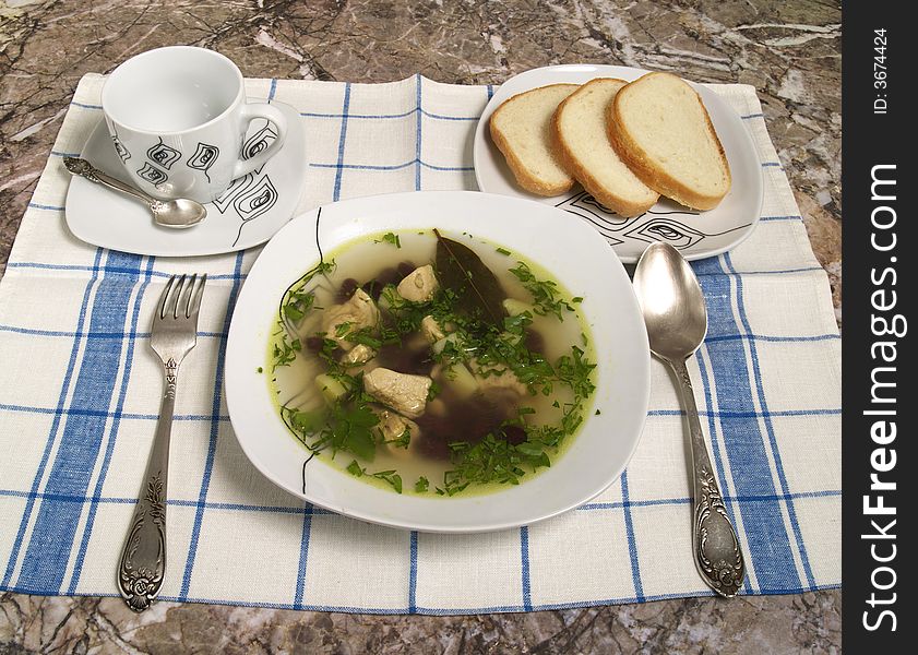 Plate of chicken soup with spoon and bread and tea cup