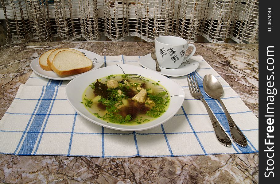 Plate of chicken soup with spoon and bread and tea cup