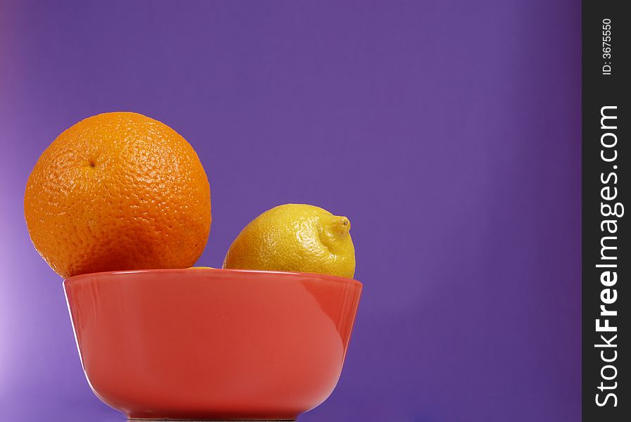 Orange and lemon in the bowl on the purple background