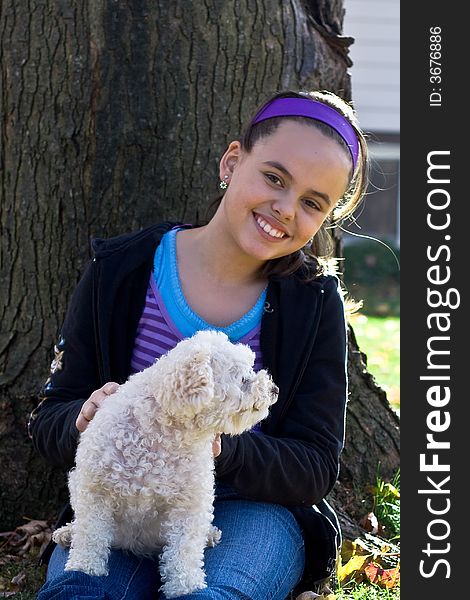 Young smiling pretty girl with white poodle outdoors in autumn sitting by tree. Young smiling pretty girl with white poodle outdoors in autumn sitting by tree