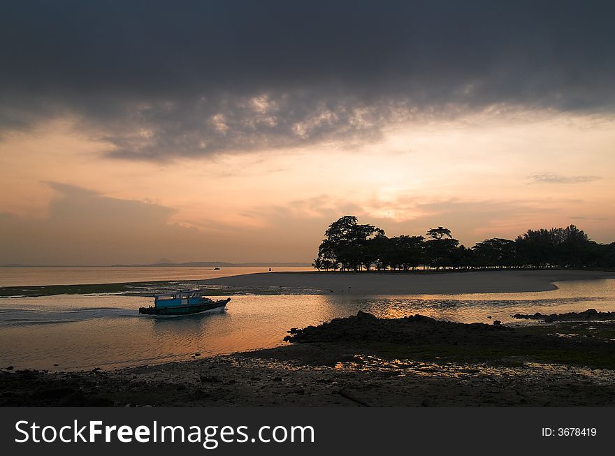 A ferry entering the mouth of a creek at low tide as the sun rises in an overcast sky behind the trees on the far shore. A ferry entering the mouth of a creek at low tide as the sun rises in an overcast sky behind the trees on the far shore.
