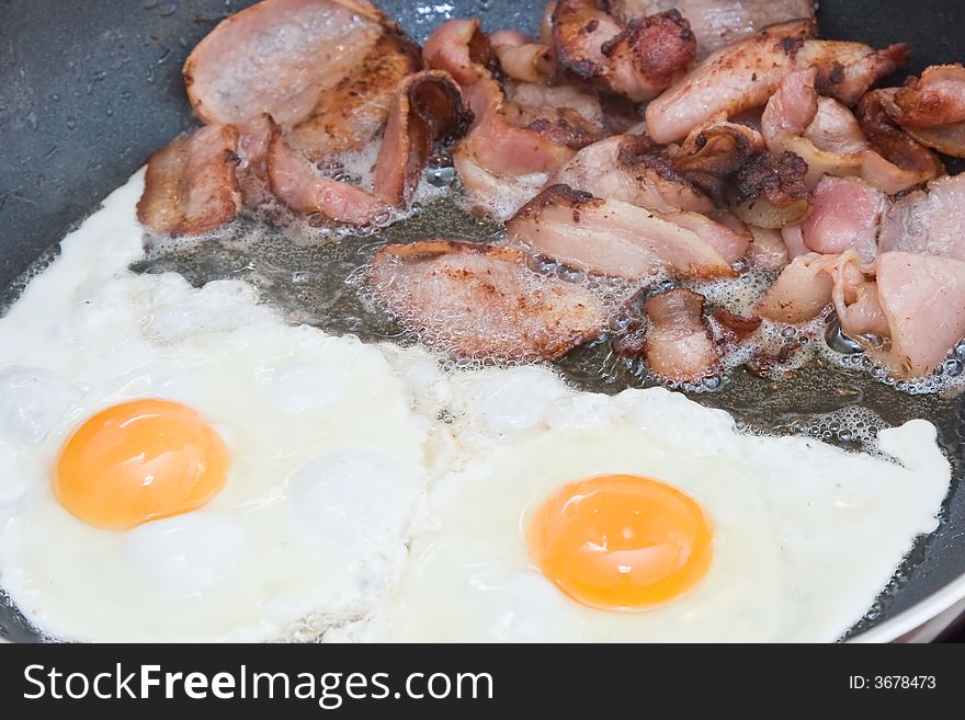 Bacon and eggs being cooked in a frying pan