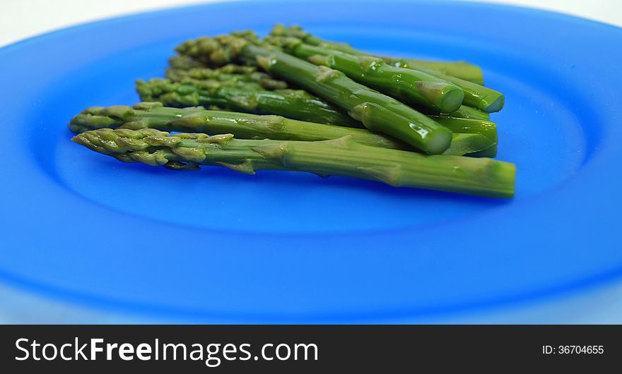 Fresh cooked asparagus spears on a bright blue plate.