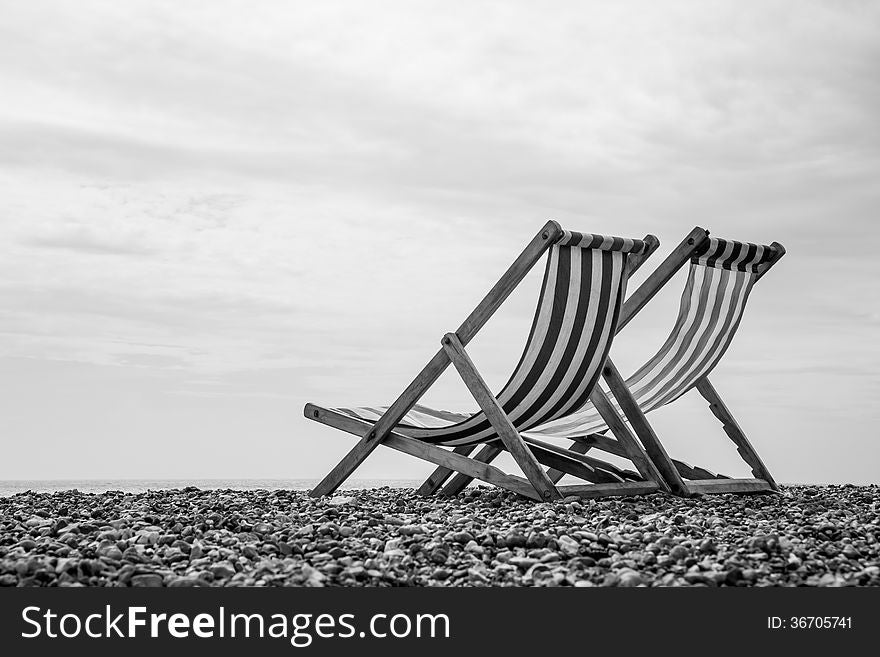 A low-angle monochrome shot of a pair of deck chairs looking out to sea. A low-angle monochrome shot of a pair of deck chairs looking out to sea