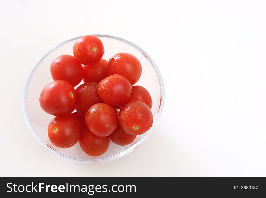 Cherry tomatoes in a transparent glass bowl on a white table-top