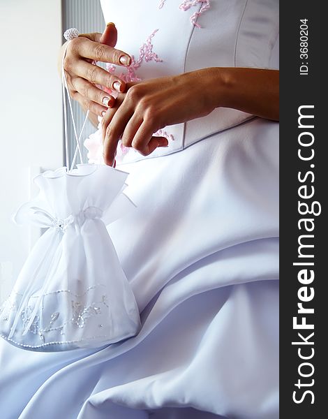 Bride with small bag in hands. She caoted in dress with pink flowers